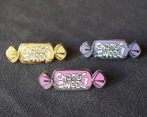 Three candy-shaped enamel pins on a dark textured background, featuring the text 'Chaotic Sweet' in white. One pin is gold, one is lavender, and one is pink, all with silver-toned metal edges.