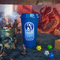Blue cup with 'Dragon's Breath' logo on a table with gaming accessories
