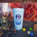 Light blue tumbler with 'Dragon's Breath' logo on a table with gaming accessories.