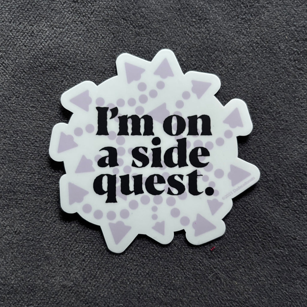 A die-cut sticker with the phrase 'I'm on a side quest.' in black serif text, surrounded by a white scalloped border with light purple geometric patterns, shown on a dark textured background.