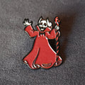 A gothic-style enamel pin depicting a skeletal figure in a flowing red robe holding a twisted staff, photographed on a textured dark gray background.